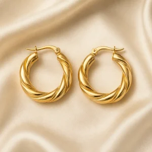 Sculptural twisted gold-tone hoop earrings on ivory satin