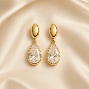 Gold-tone pear-shaped gemstone-style drop earrings on ivory satin