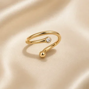 Open gold-tone orbit ring with a clear stone on ivory satin