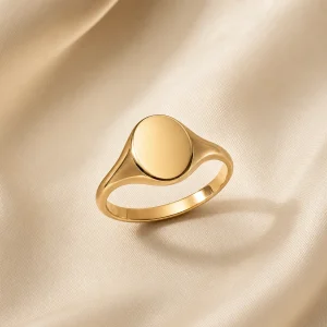 Minimal polished gold-tone oval signet ring on ivory satin